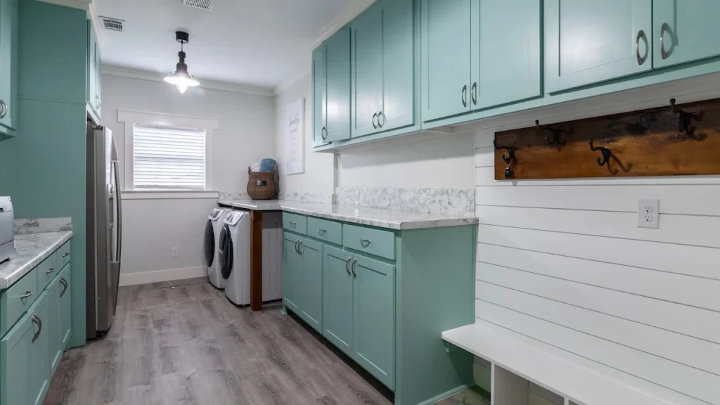 Modern laundry room with mint green cabinets, marble countertops, and washer and dryer units.