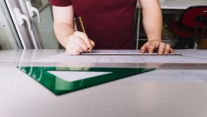 Person drawing architectural plans with pencil and ruler on blueprint at drafting table