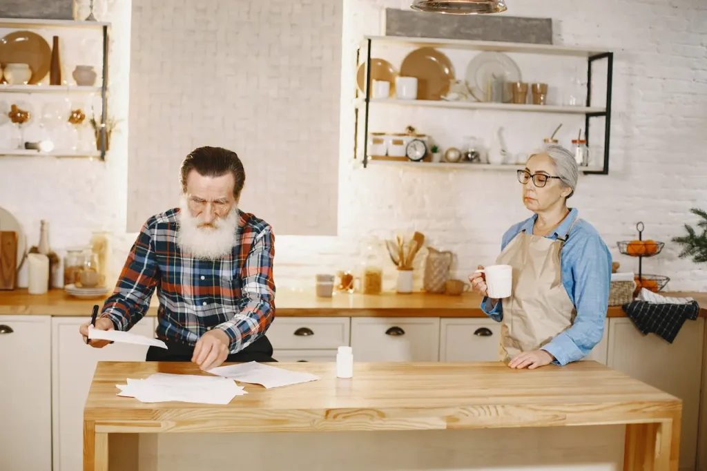 Senior couple reviewing documents at a kitchen table while the woman drinks coffee