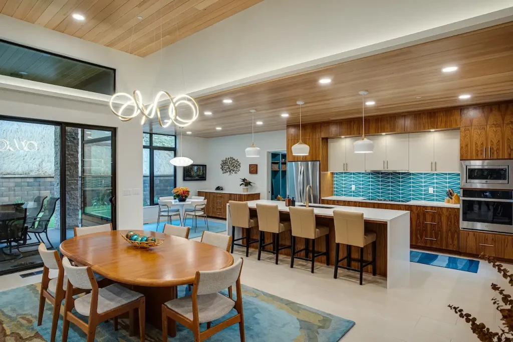 Modern open-concept kitchen and dining area with large island, wood cabinets, and blue tile backsplash