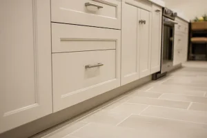 Close-up of modern white kitchen cabinets with drawers and light tile flooring