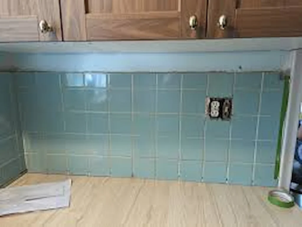 Blue kitchen tile backsplash installation under wooden cabinets with exposed electrical outlet