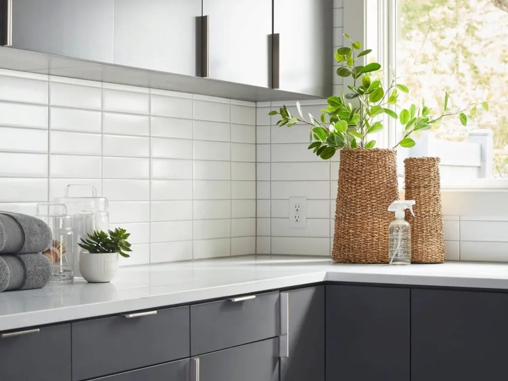 Modern kitchen corner with white subway tile backsplash, gray cabinets, and decorative plants on the countertop