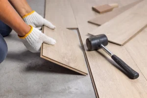 Worker installing laminate wood flooring using rubber mallet during home renovation