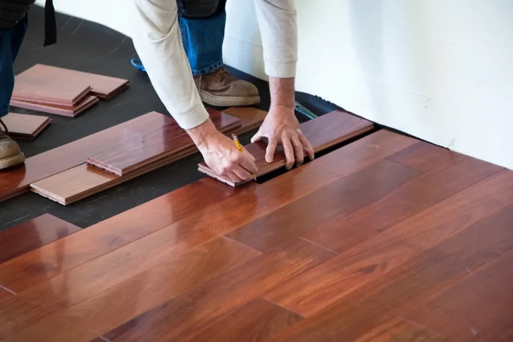 Worker measuring and installing hardwood flooring planks during home renovation