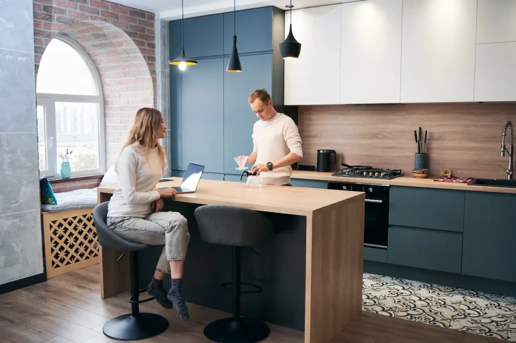 Modern kitchen with island where couple multitasks between cooking and working on a laptop